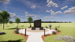 A picture of the ground and blue sky with white crowds and in the middle of the picture a black granite memorial with two people walking around it.